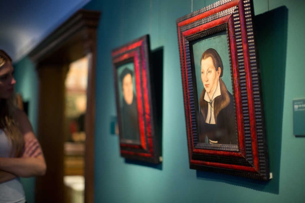 Zwei Bilder, die an der Wand im Ausstellungsraum des Museums Ludwig-Roselius in Bremen hängen. Zu sehen ist eine Frau, die das Porträt von Katharina von Bora anschaut. Im Hintergrund ist ein Porträt von Martin Luther zu sehen.