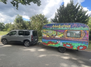 buntbemalter Wohnwagen der von einem silbernen Van gezogen wird